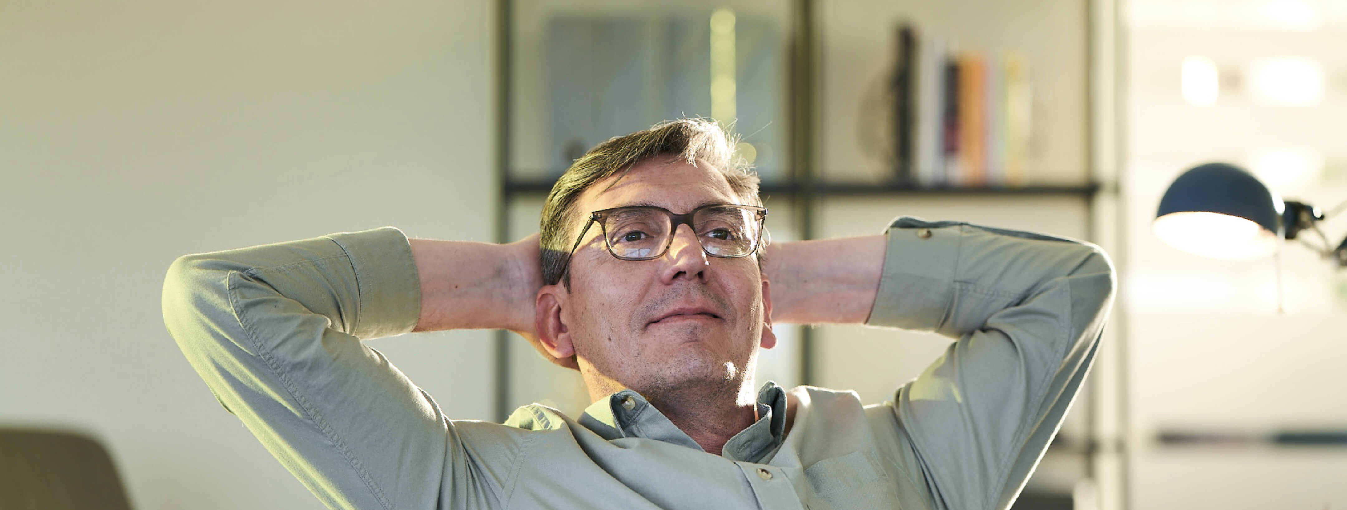 A middle-aged man relaxes in his chair with his hands behind his head.