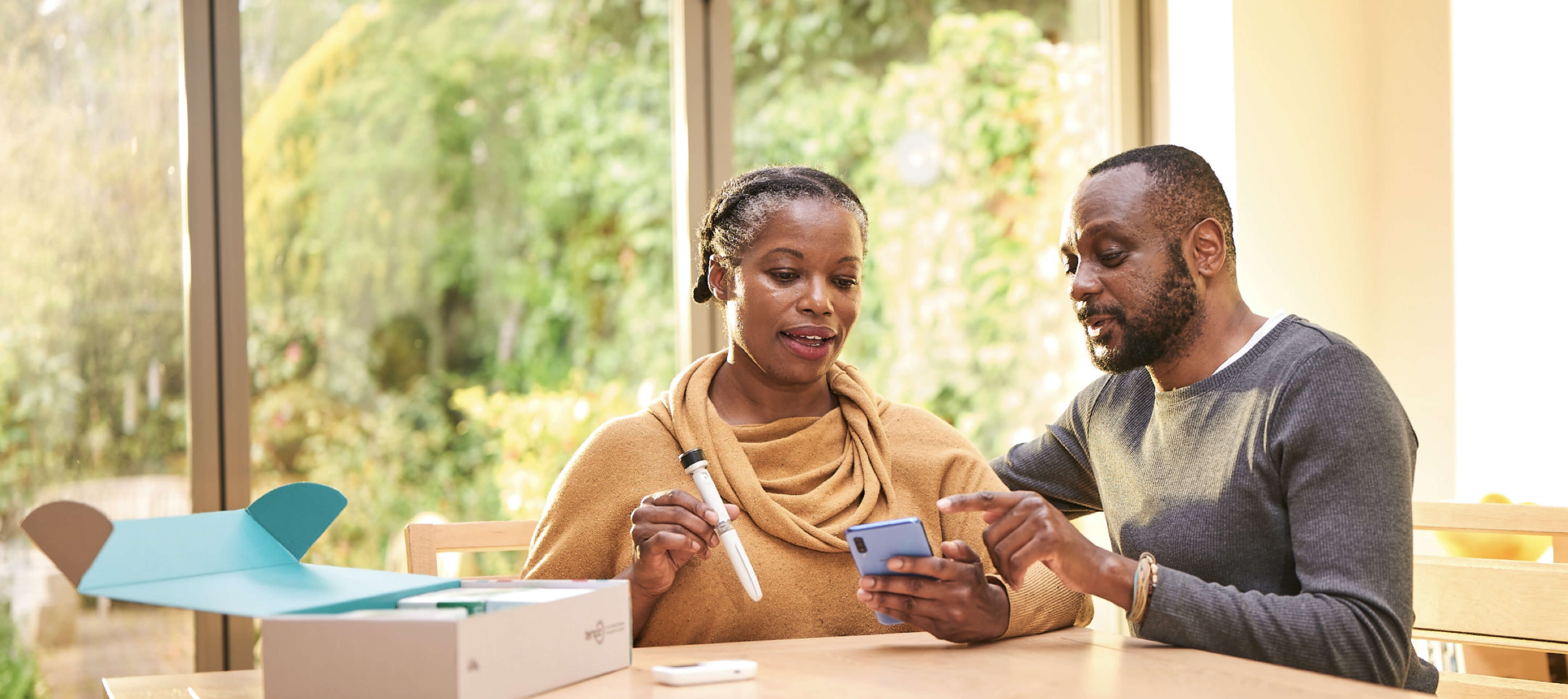 A middle aged man and women sit in conversation at their kitchen table. The woman has the Tempo Pen and Tempo Smart Button in her right hand, the man is pointing at the screen of the smartphone in her left hand