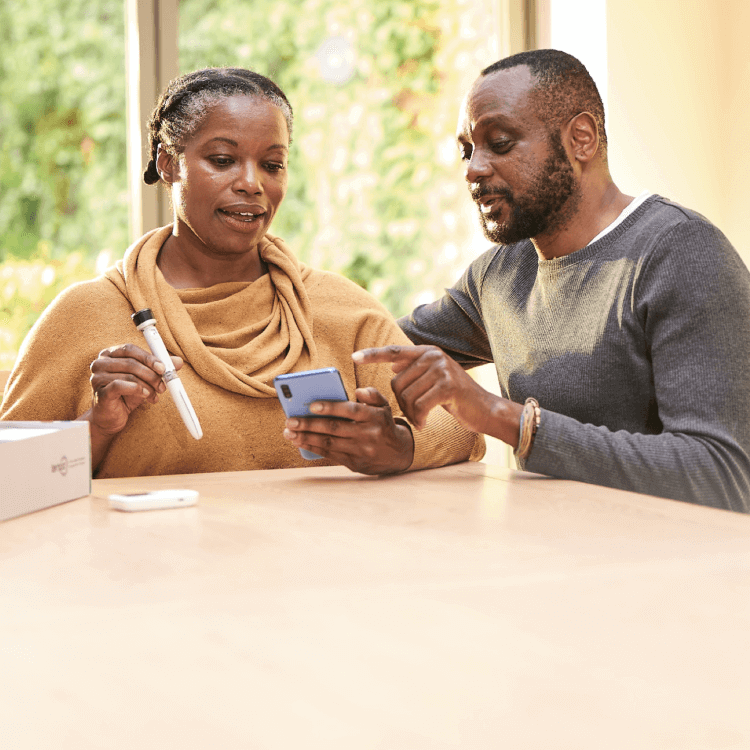 A middle aged man and women sit in conversation at their kitchen table. The woman has the Tempo Pen and Tempo Smart Button in her right hand, the man is pointing at the screen of the smartphone in her left hand