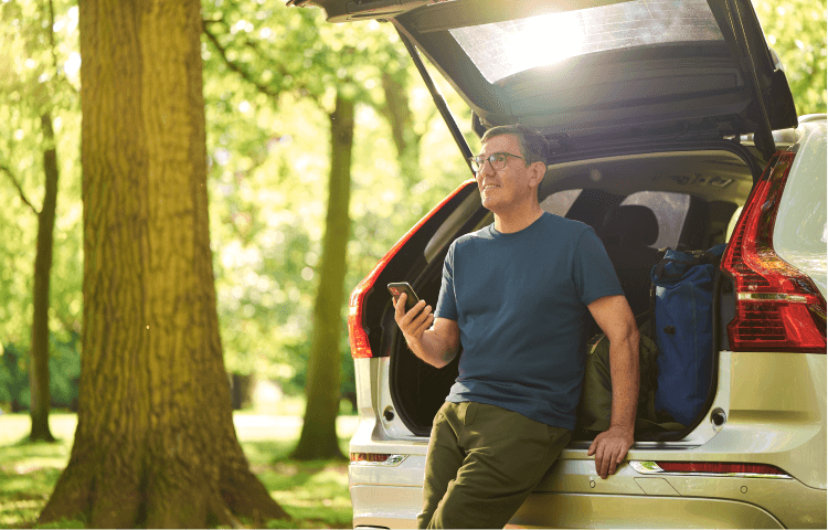 A middle-aged man, with his smartphone in hand, takes in the scenery as he sits in the trunk of his SUV.