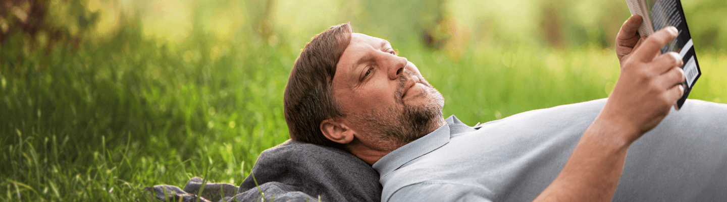 A man reads a book while lying on his back in a field.