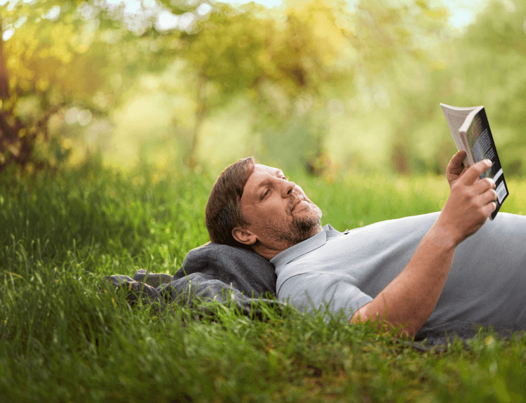 A man reads a book while lying on his back in a field.