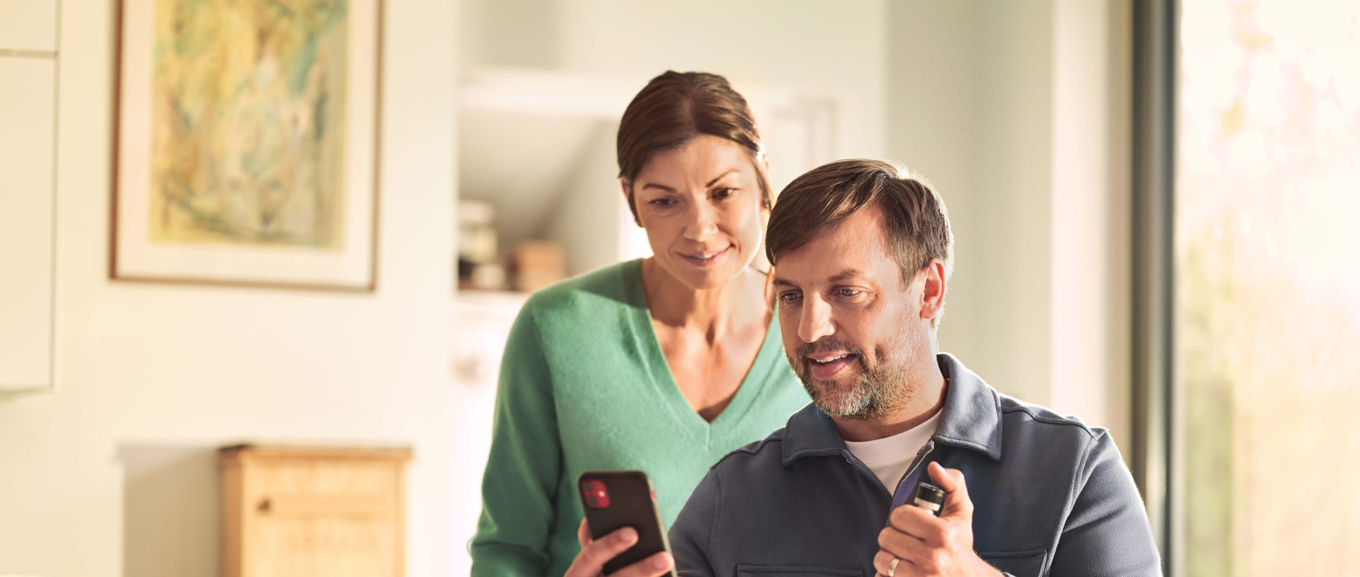 Middle-aged man with a cell phone in his hand. Woman looks over his shoulder.