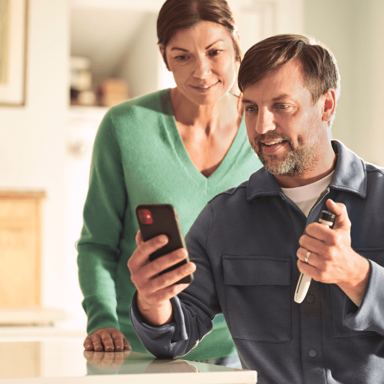 Middle-aged man with a cell phone in his hand. Woman looks over his shoulder.