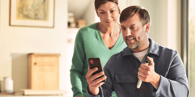 Middle-aged man with a cell phone in his hand. Woman looks over his shoulder.