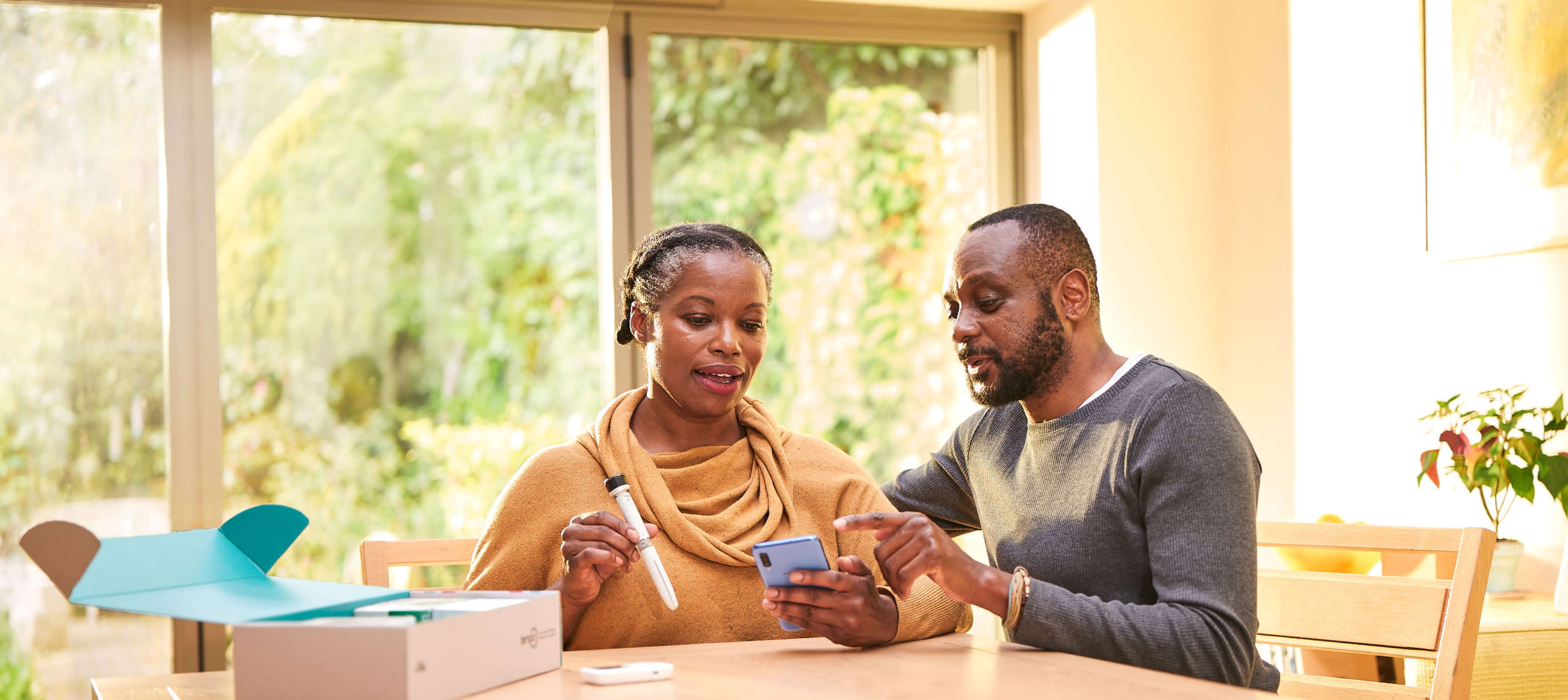 A middle aged man and women sit in conversation at their kitchen table. The woman has the Tempo Pen and Tempo Smart Button in her right hand, the man is pointing at the screen of the smartphone in her left hand