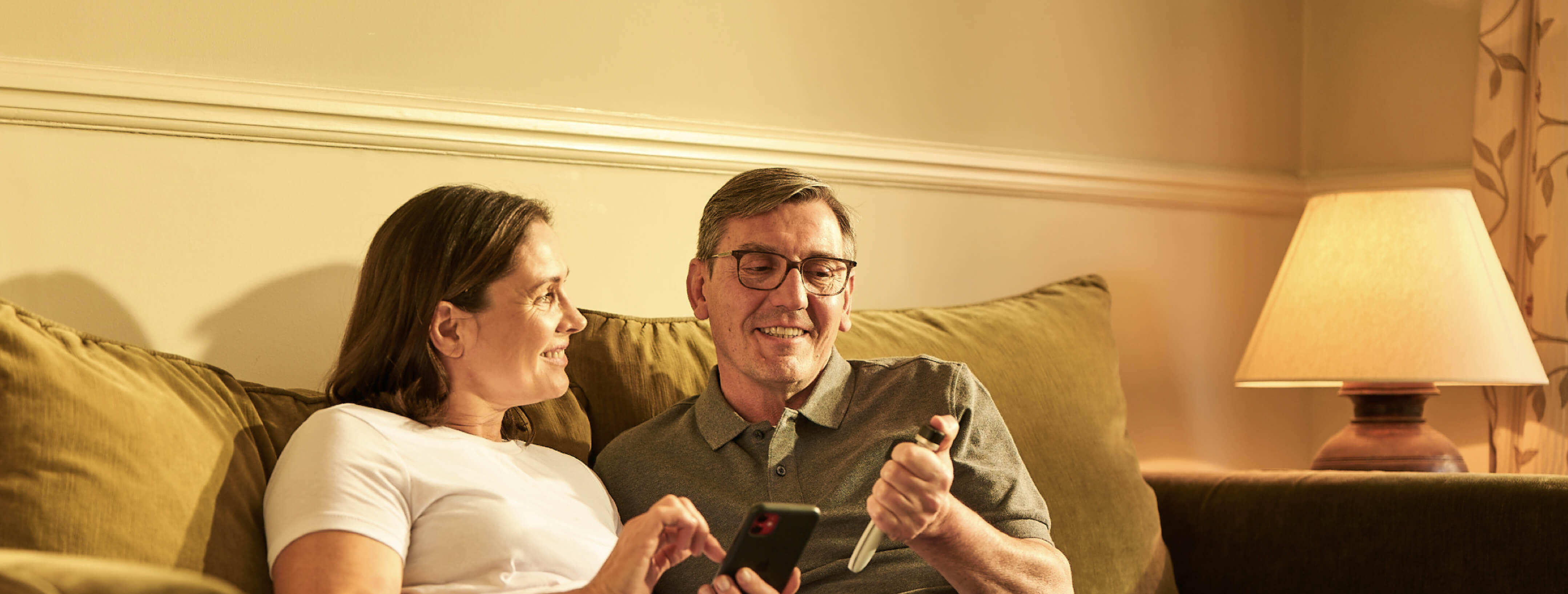 A middle-aged man and woman sit on their couch; the woman holds a smartphone while the man looks at a Tempo Pen with Tempo Smart Button attached.