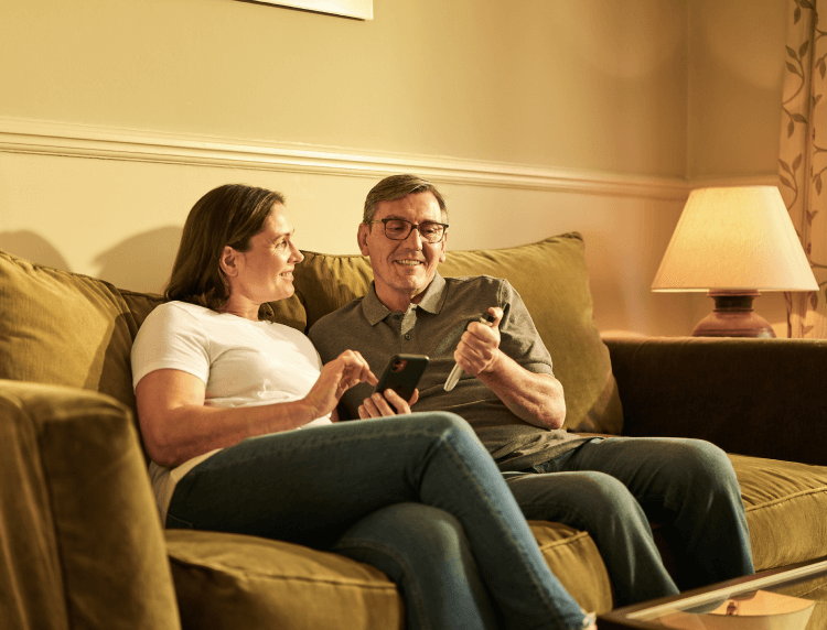 A middle-aged man and woman sit on their couch; the woman holds a smartphone while the man looks at a Tempo Pen with Tempo Smart Button attached.