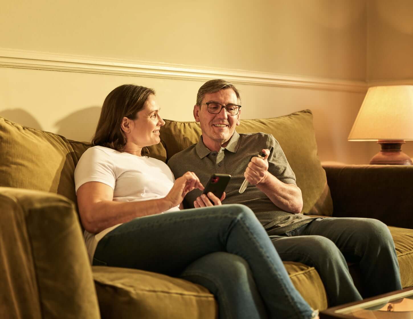 A middle-aged man and woman sit on their couch; the woman holds a smartphone while the man looks at a Tempo Pen with Tempo Smart Button attached.
